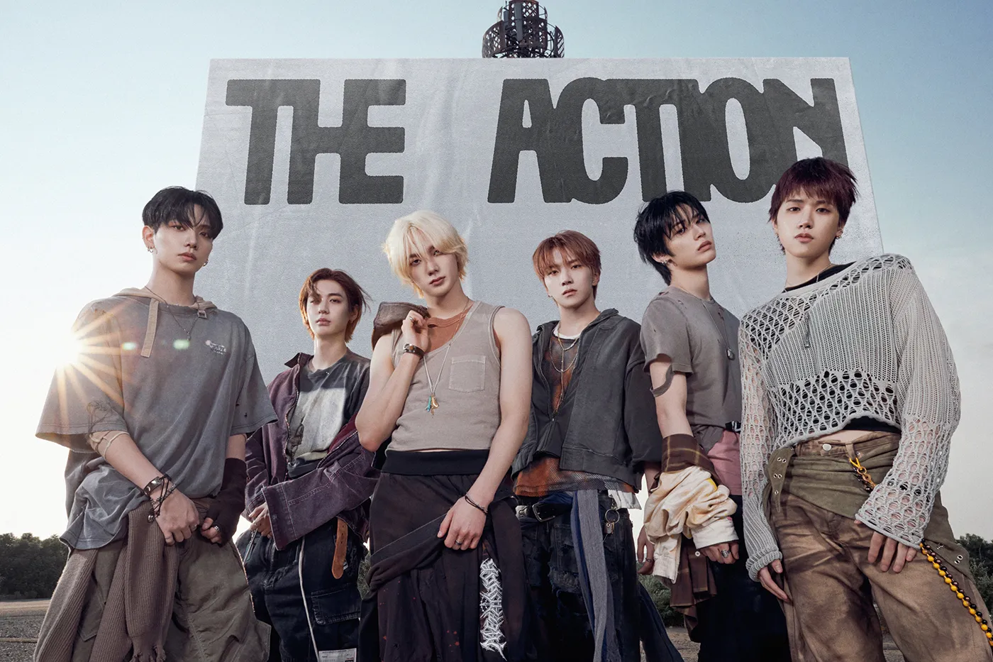 BOYNEXTDOOR, a six-member South Korean boy group, standing together in front of a large sign that reads 'THE ACTION', dressed in casual, stylish outfits.