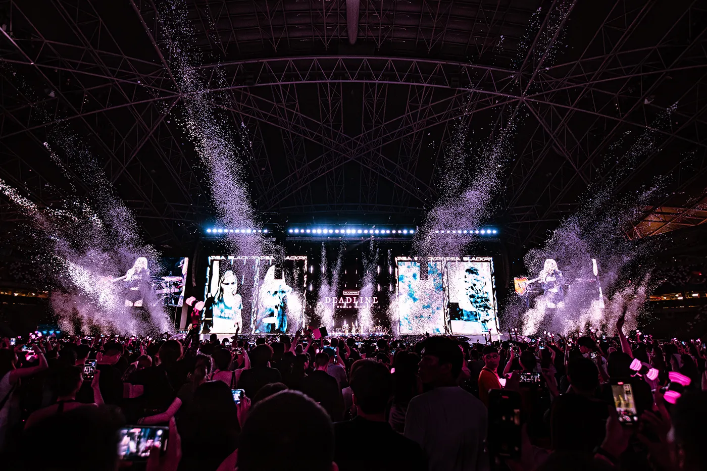 PHOTO BLACKPINK DEADLINE SINGAPORE 2025: A large crowd at a BLACKPINK concert in a stadium, with vibrant lights, confetti, and large screens displaying images of the performers.