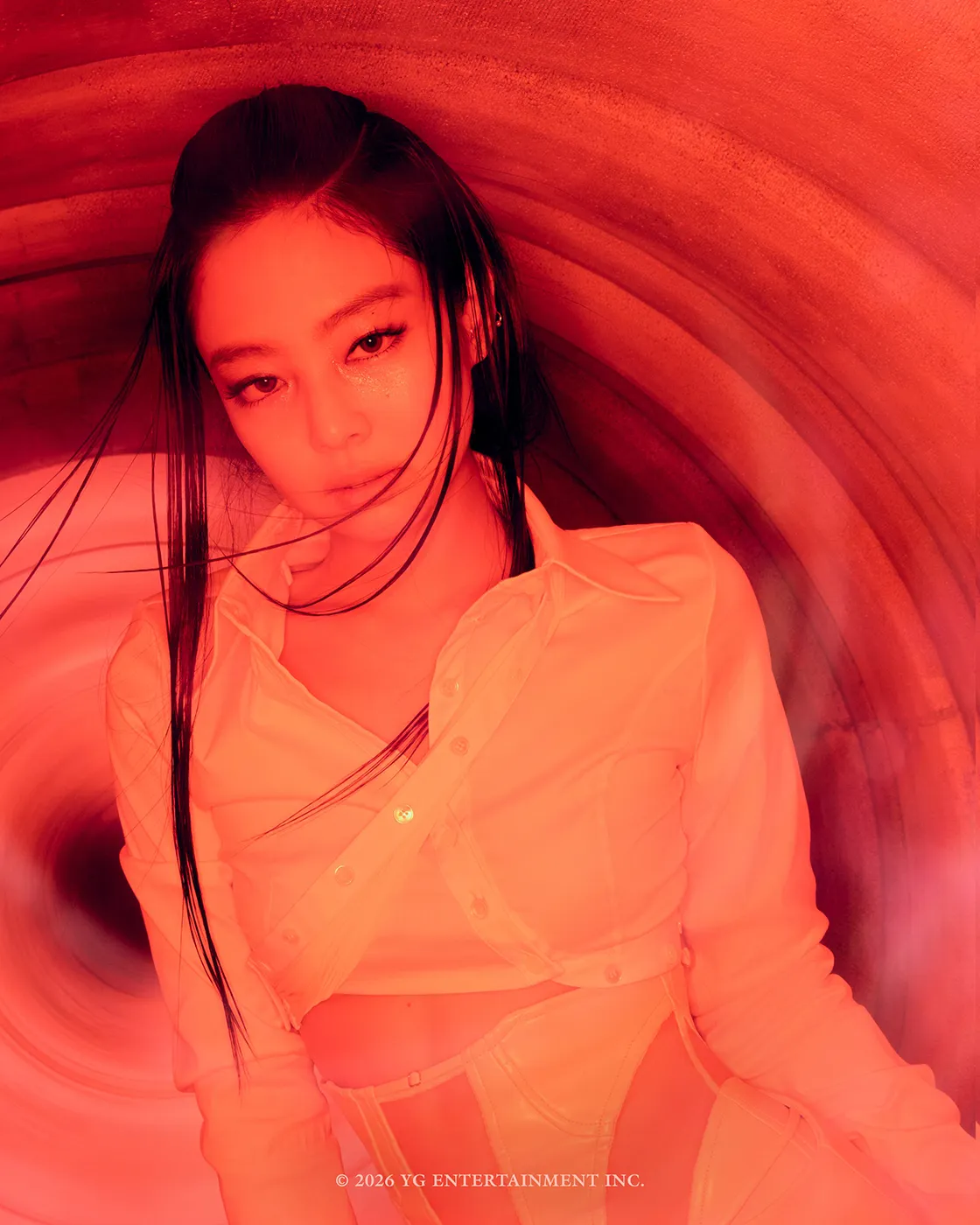 A young woman with long black hair is looking directly at the camera, set against a swirling red background. She is wearing a white cropped shirt that highlights her midriff.