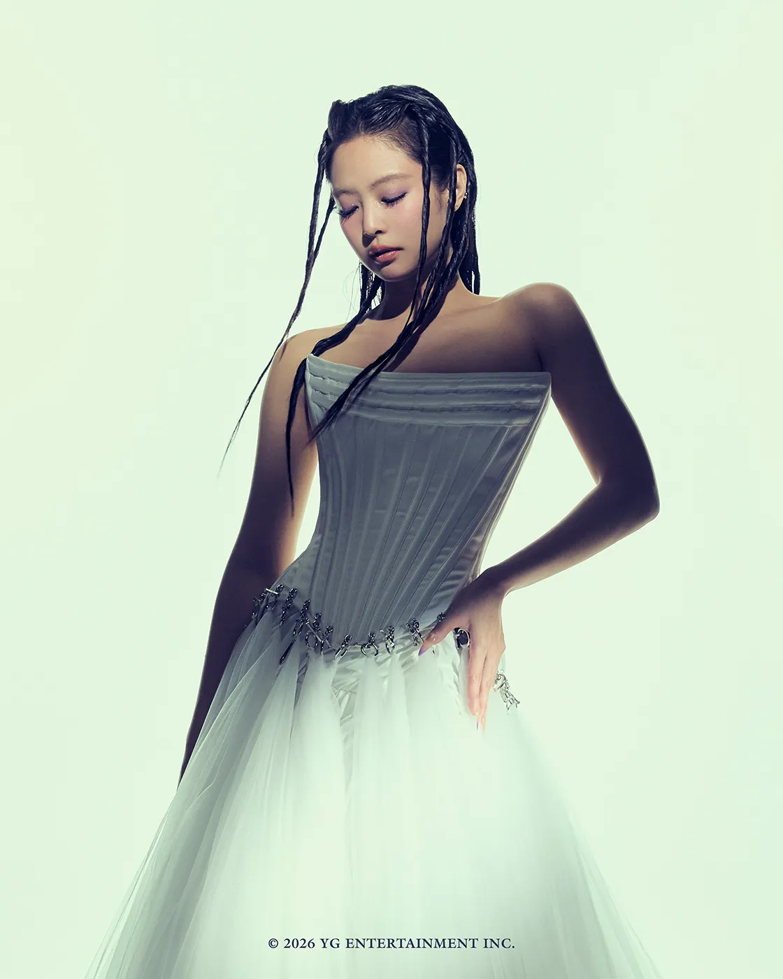 A woman in a white strapless gown with delicate detailing, standing gracefully with her head slightly bowed and eyes closed, against a light background.