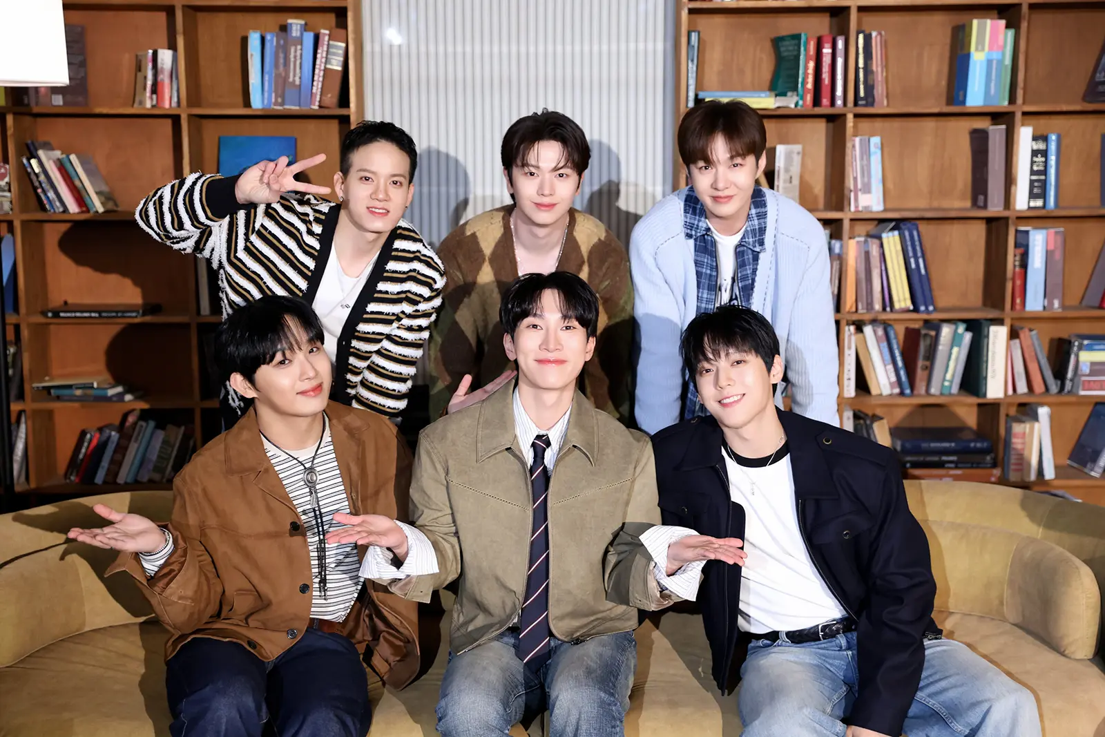 BTOB members for We Together Single Album. A group of six young BTOB Members posing together in a cozy room with bookshelves in the background. They are smiling and making playful gestures, dressed in casual and stylish outfits.