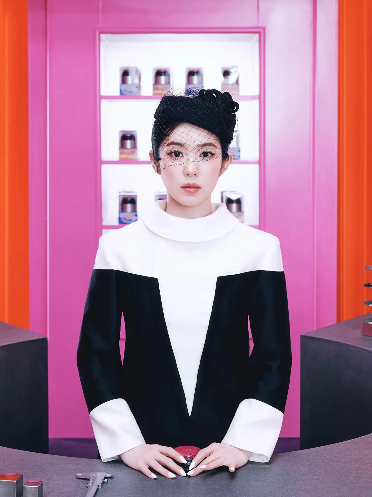 IRENE Teaser for 1st Album Biggest Fan. Irene in a black and white outfit with a decorative veil poses in a vibrant pink room, surrounded by beauty products on a counter.