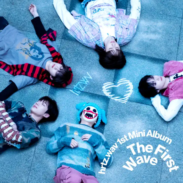 Five members of a music group lying on the ground surrounded by colorful outfits and playful expressions, with text overlay that includes 'hrtzwav 1st Mini Album The First Wave'.
