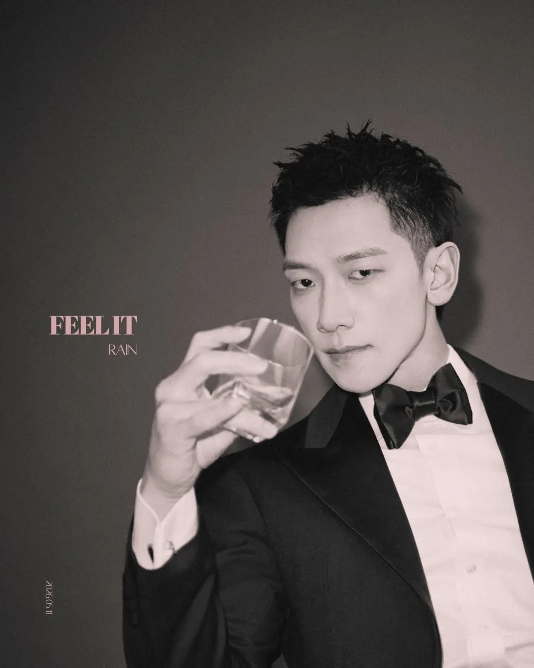 Teaser for RAIN Digital Single – Feel It (2026). A man in a formal black tuxedo holding a glass of whiskey, with a serious expression and short dark hair. The background is softly lit, enhancing a sophisticated ambiance.