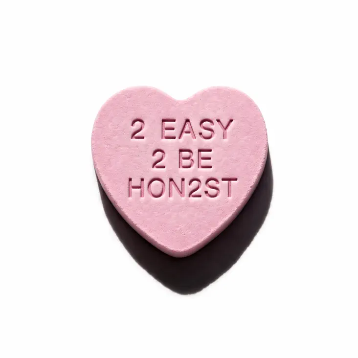 Lee Hi Single – 2 EASY 2 BE HON2ST (2026). A pink heart-shaped candy with the text '2 EASY 2 BE HON2ST' imprinted on its surface.