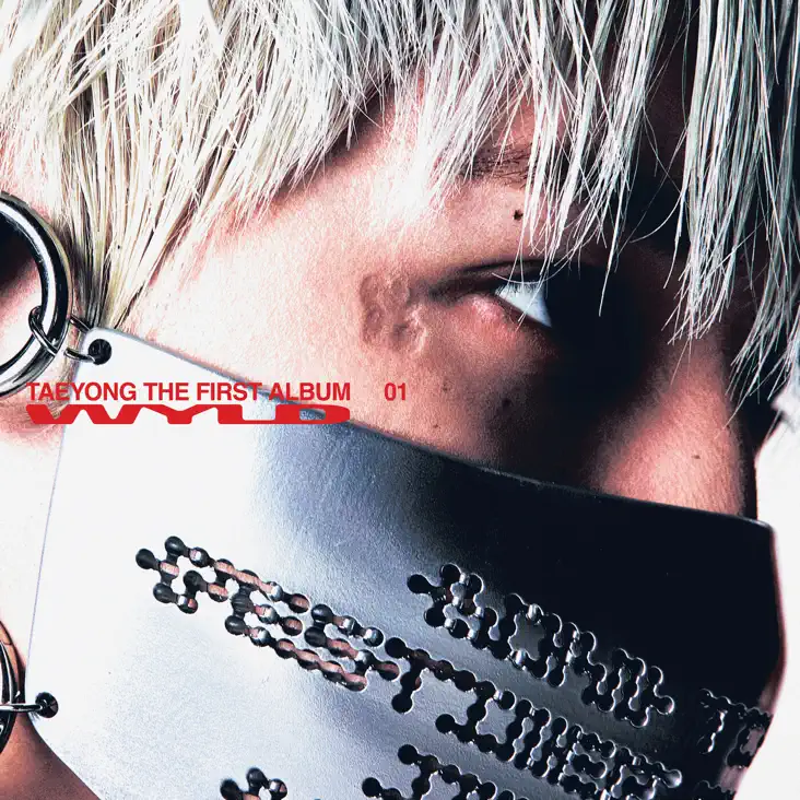 Close-up of a person's face with platinum blonde hair, wearing a silver mask. Text overlay reads 'TAEYONG THE FIRST ALBUM WYLD (2026) Album Cover Art