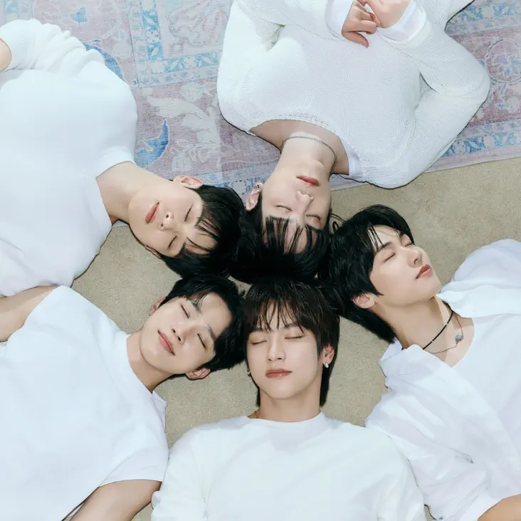 N.Flying In Between Seasons Album Cover. Four young men lying in a circle on a light-colored rug, with their eyes closed and heads touching at the center.